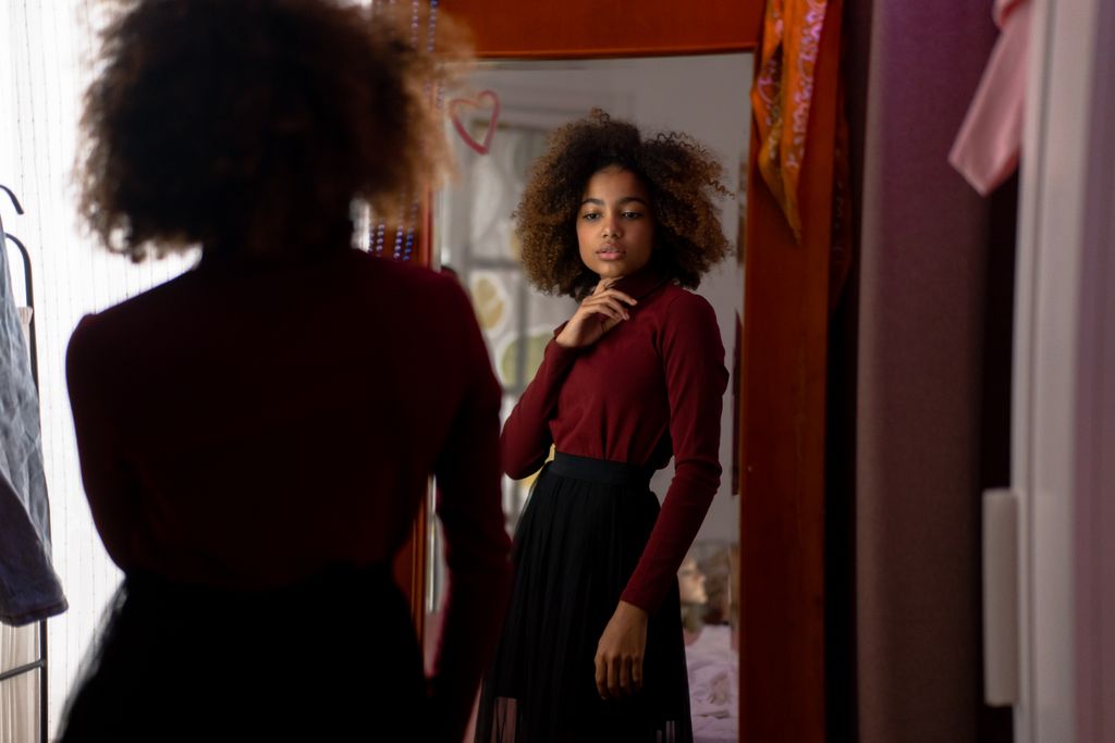 Young woman with afro hairstyle posing stylishly indoors in front of a mirror.