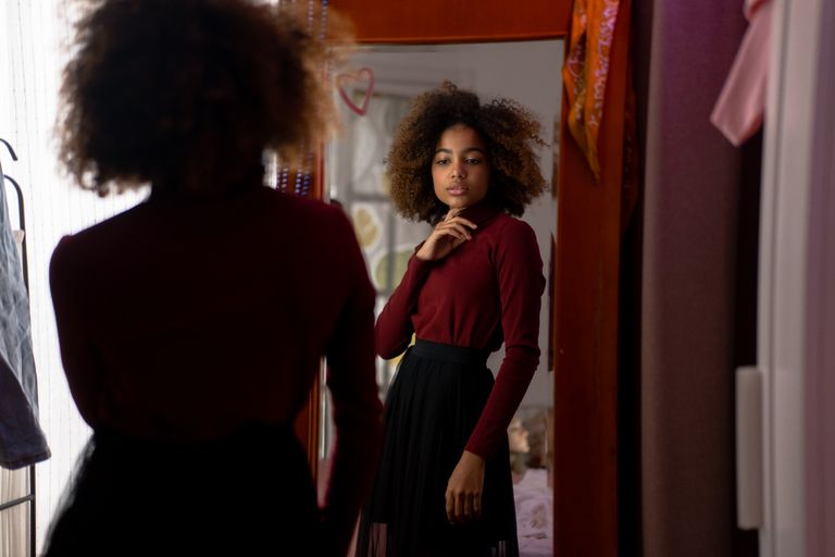 Young woman with afro hairstyle posing stylishly indoors in front of a mirror.