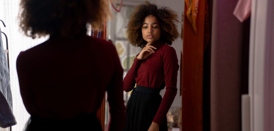 Photo by cottonbro studio Young woman with afro hairstyle posing stylishly indoors in front of a mirror.